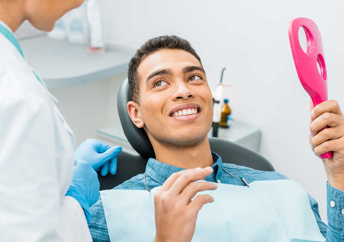 A male patient smiling at the dentist with a mirror in his hand